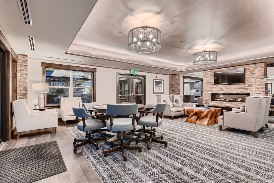 Well-lit lounge area with a round game table and chairs, armchairs and sofas arranged around a fireplace and wall-mounted TV.