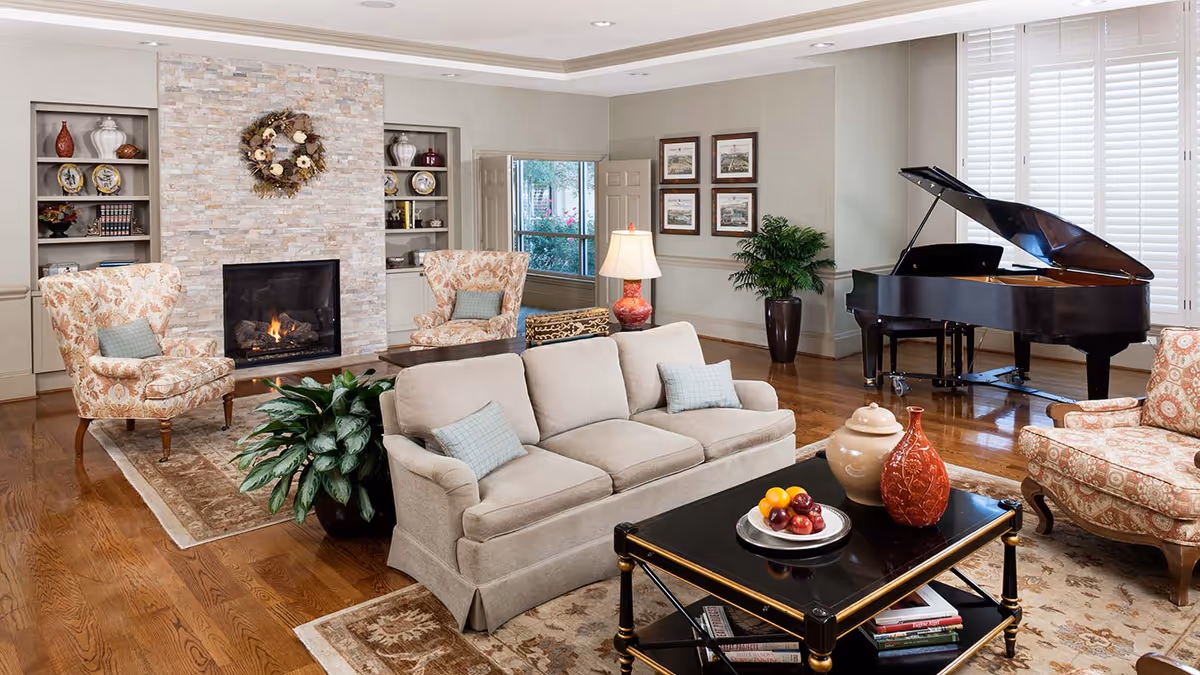 Bright, well-appointed living room with a sofa and armchairs arranged around a coffee table and fireplace, with a grand piano in the background.