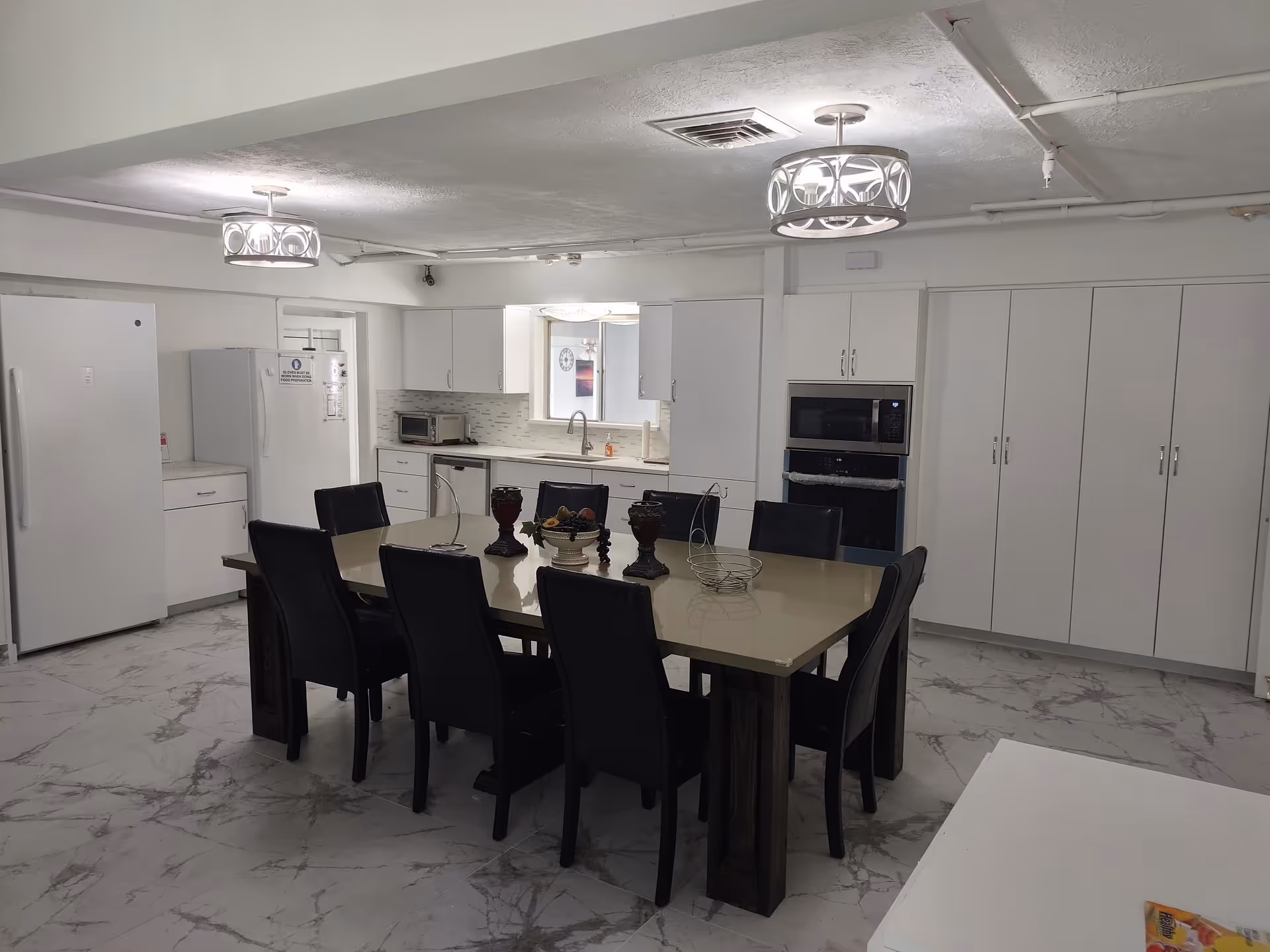 Open kitchen and dining area with a large rectangular table surrounded by black chairs, white cabinets, and appliances.