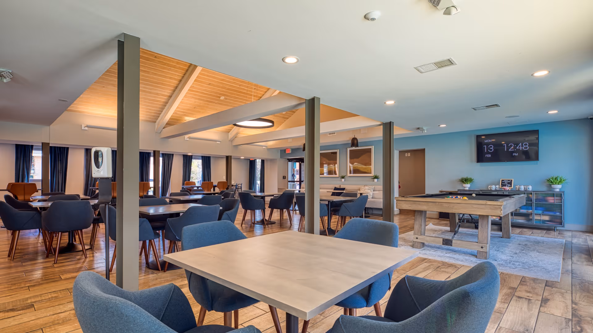Spacious senior living common room with multiple tables and chairs, a pool table, and a wall-mounted TV.