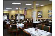 Dining room with neatly set tables and chairs, columns, framed artwork, and an American flag on the wall.