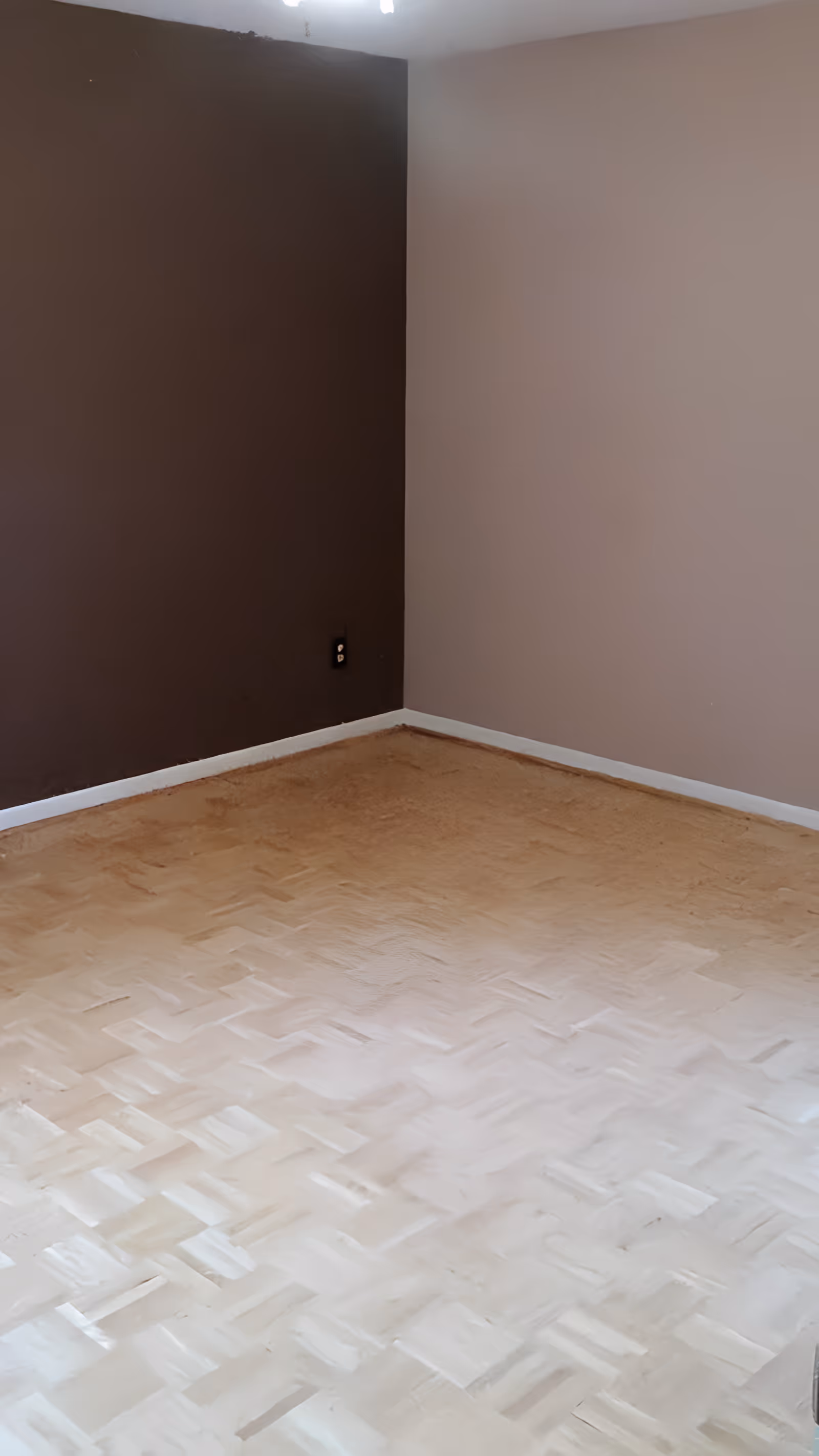 Empty room corner with two walls painted in different colors, one dark brown and the other light beige, and a light-colored wooden parquet floor.