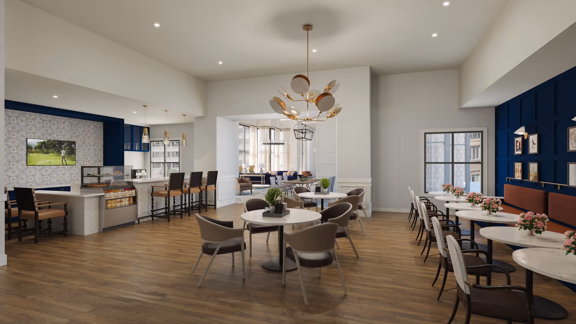 A spacious and modern dining area with round tables and chairs arranged neatly. The room features wooden flooring, a stylish chandelier, and a blue accent wall with framed artwork. There is a counter with bar stools and a television mounted on a patterned wall. Large windows allow natural light to brighten the space.