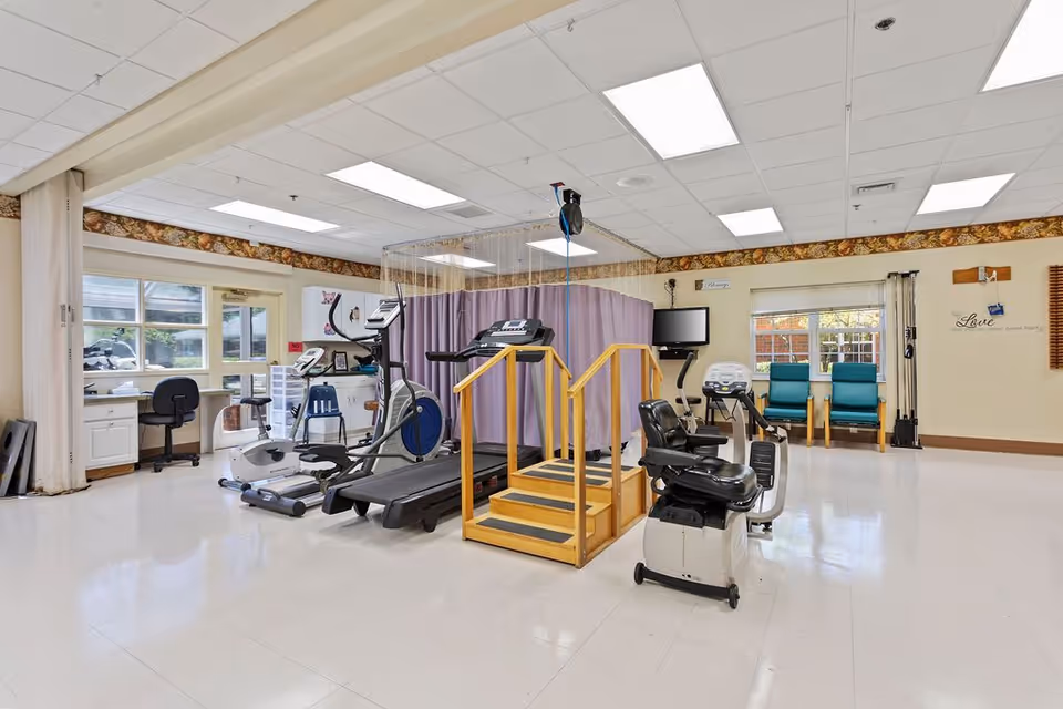 Bright rehabilitation gym interior with treadmills, exercise bikes, parallel bars and seating.