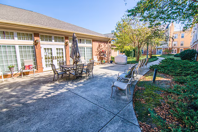 Outdoor patio area at Brookdale Jones Farm featuring a dining table with chairs, umbrellas, and landscaped greenery.