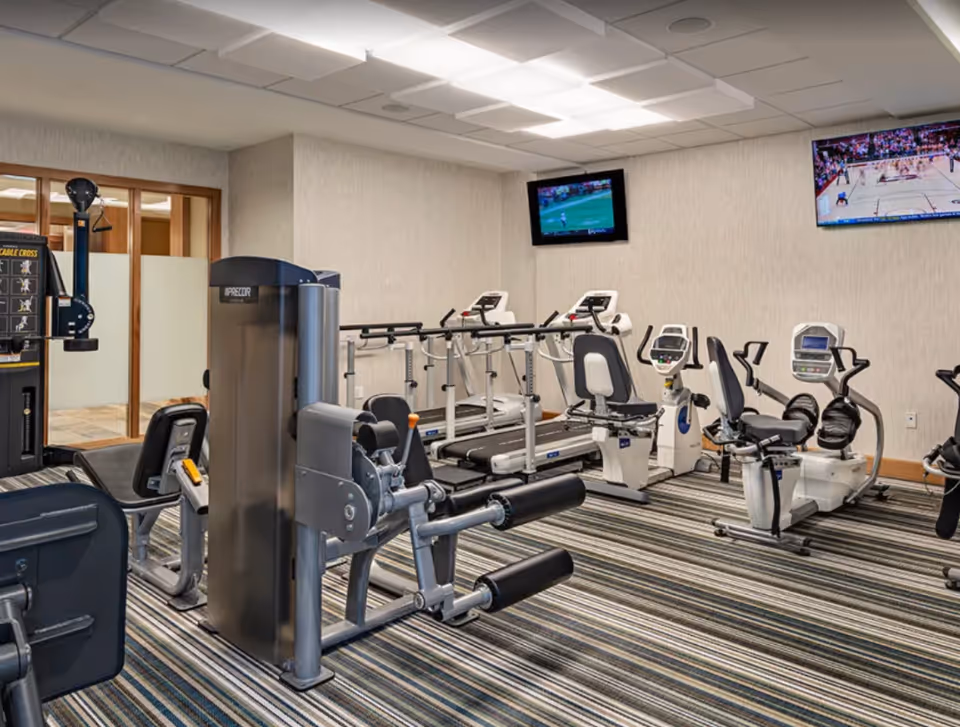 A fitness room with strength machines, treadmills and recumbent bikes and wall-mounted TVs.