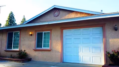 A single-story beige house with a white garage door and two front windows.