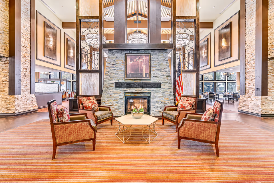 Spacious communal lounge with armchairs arranged around a central stone fireplace and large windows.