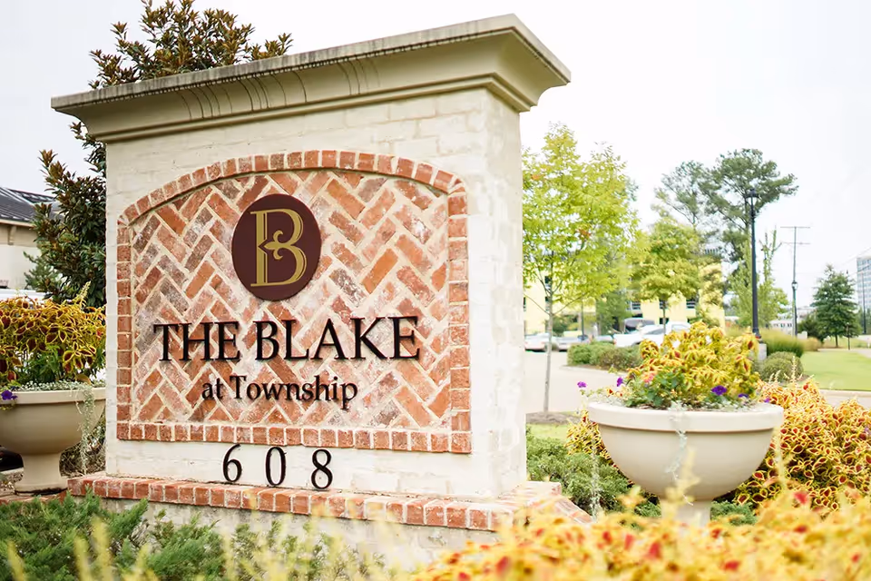Stone entrance sign reading "The Blake at Township" with the address "608" surrounded by planters and landscaping.