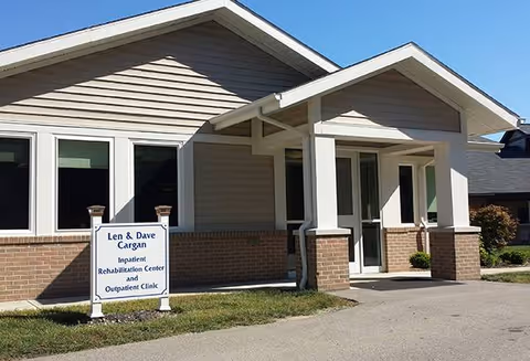 Front view of a beige assisted living facility with a covered entrance and sign.