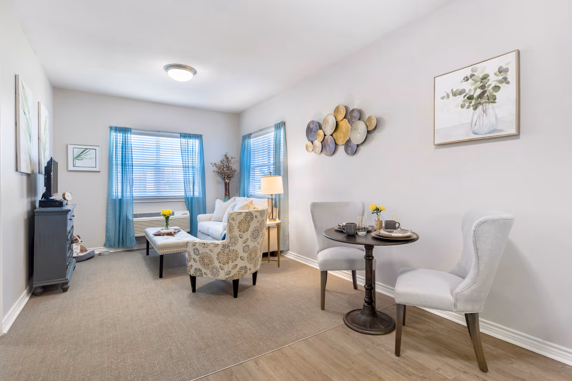 Furnished living room with armchairs, a small round dining table, coffee table, TV stand, and blue-curtained windows.