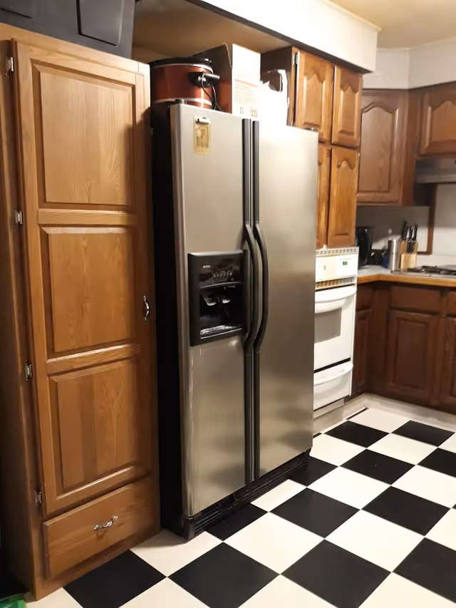 Stainless steel side-by-side refrigerator between wooden cabinets in a kitchen with a black-and-white checkered floor.