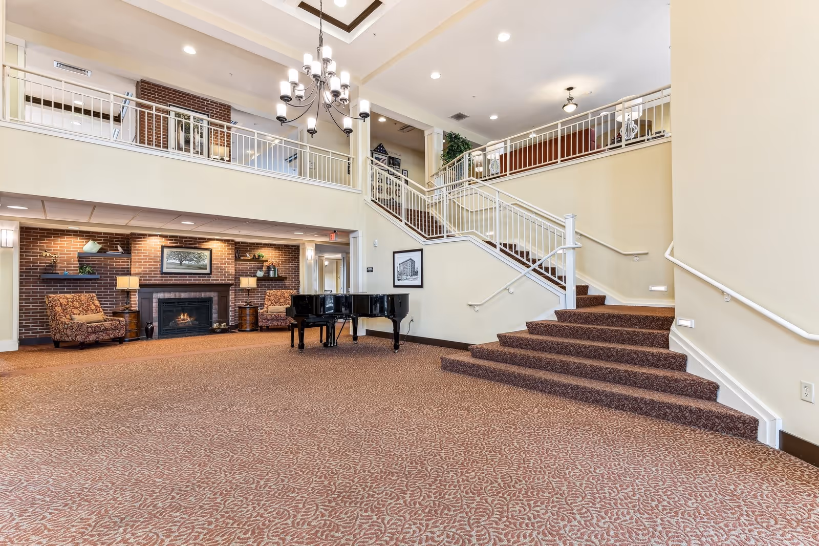 Spacious two-story lobby with a staircase, grand piano, fireplace, seating area, and chandelier.