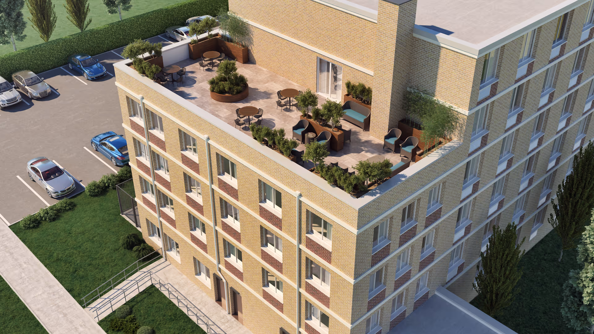 Aerial view of a multi-story brick building with a furnished rooftop terrace, adjacent parking lot, and surrounding landscaping.