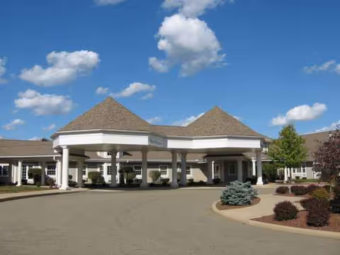 Nursing facility entrance with a porte-cochere, drive, and landscaped front under a blue sky.