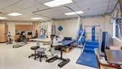 Interior rehabilitation gym in a senior facility with therapy equipment, stairs, and mats.