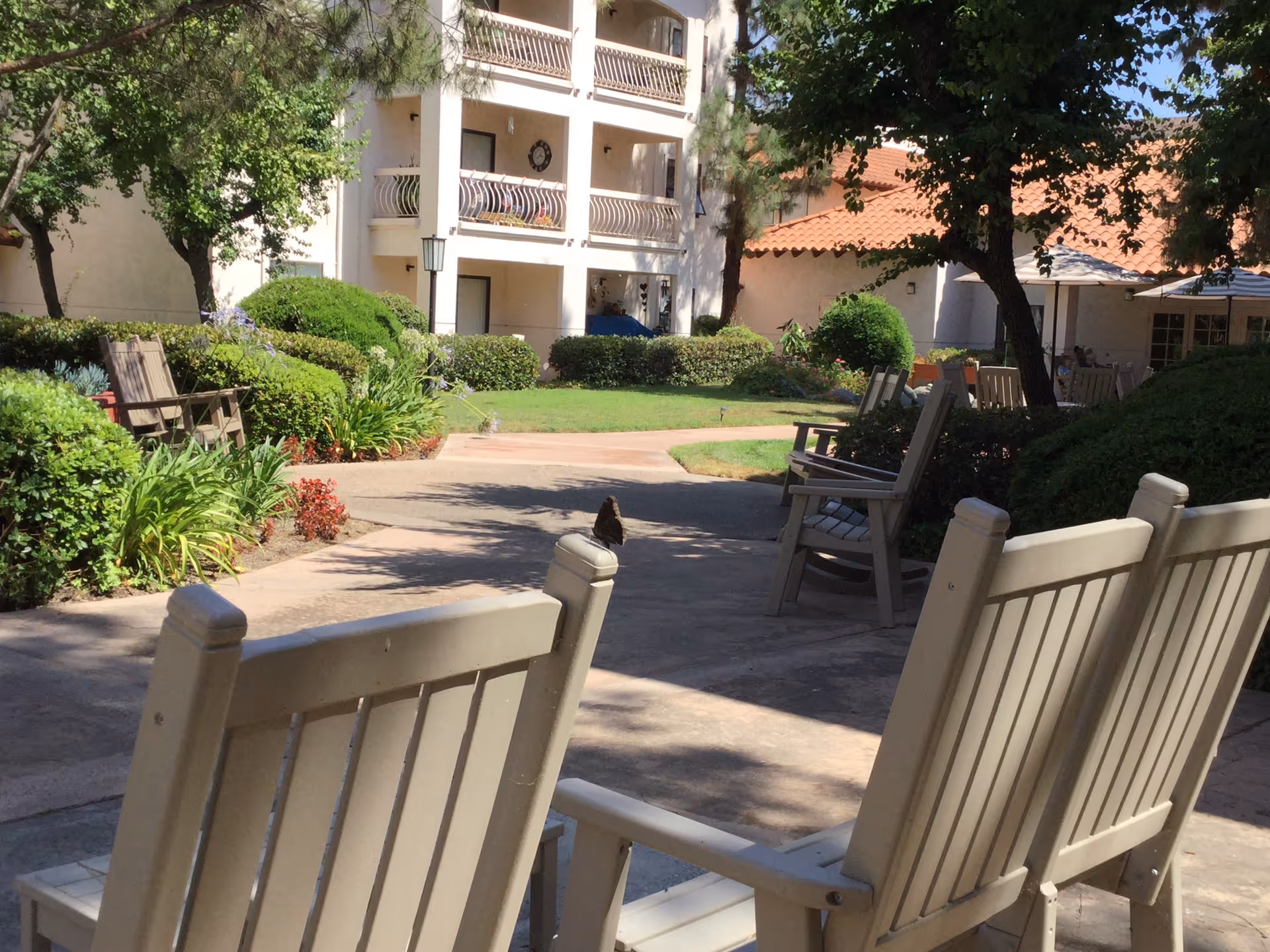 Courtyard with patio chairs, landscaped bushes and a multi-story building with balconies.