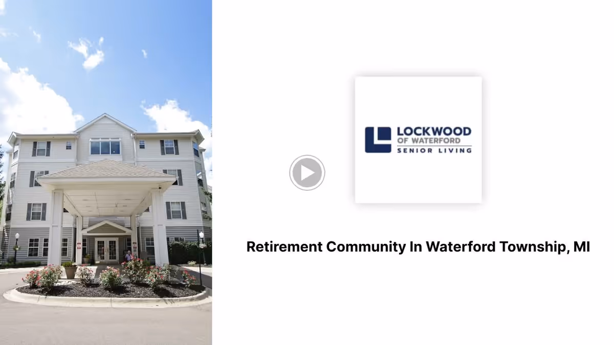 Exterior front view of a multi-story senior living facility building with a covered entrance, surrounded by landscaping and a clear blue sky with some clouds.