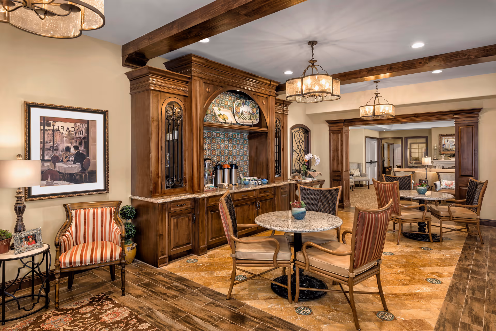 Warm communal dining and seating area with round tables, upholstered chairs, wooden cabinetry and chandeliers.