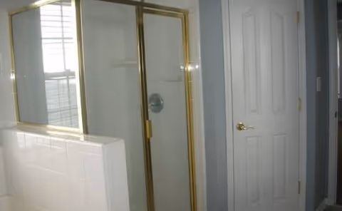 Bathroom with glass shower enclosure, tiled walls, and a white door.