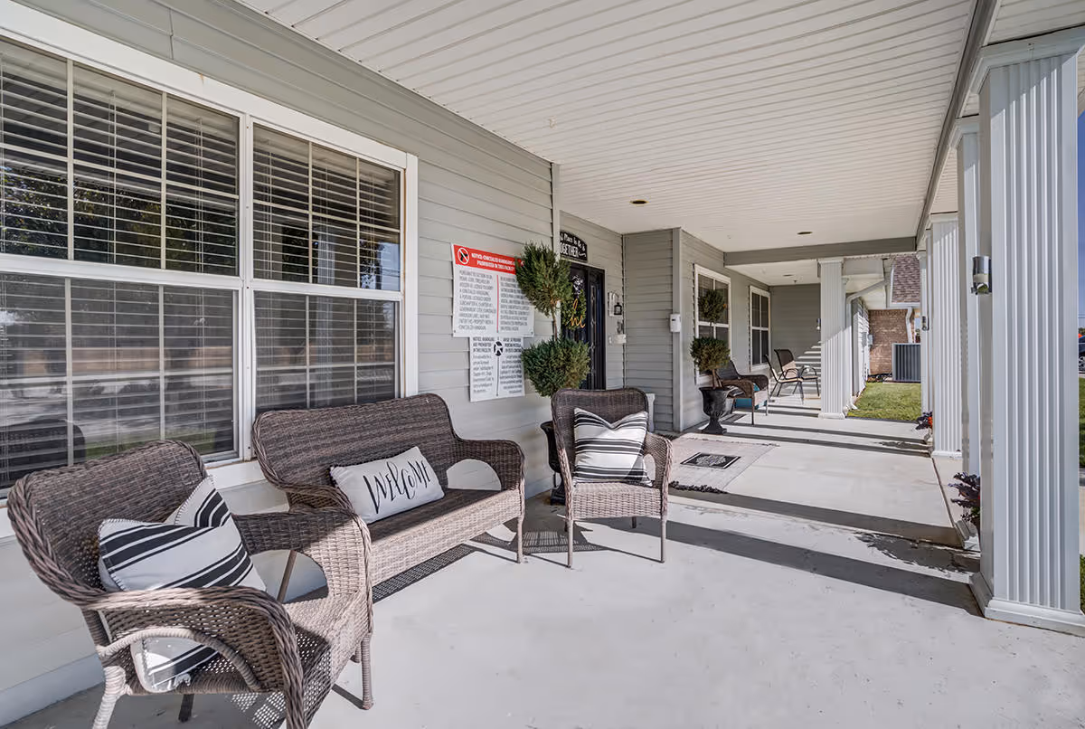 Covered front porch of Meredith Court with wicker seating, potted plants, and columns leading to multiple entrance doors.