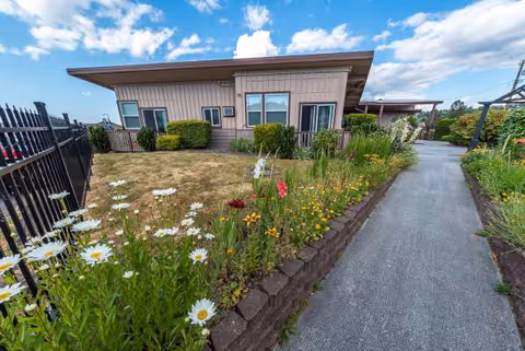 Single-story senior care facility with a garden path and blooming flower beds.