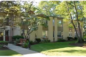 Two-story beige nursing home facade with green lawn and trees.