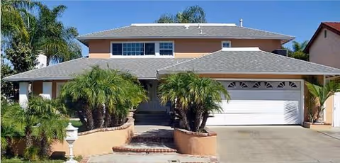 Two-story senior living facility exterior with driveway, palm trees, and a double garage.