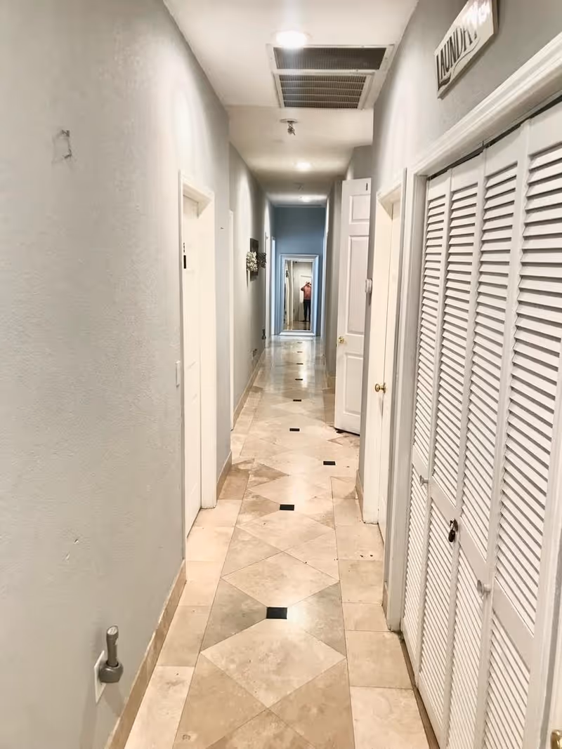 Long tiled hallway inside a residential care home with doors on both sides and a laundry closet.