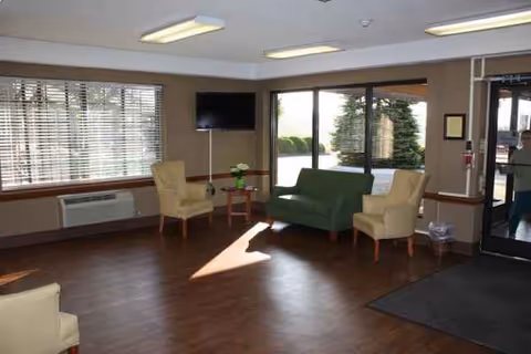 Interior lounge with chairs, a sofa, a table, and a TV in a senior living facility.