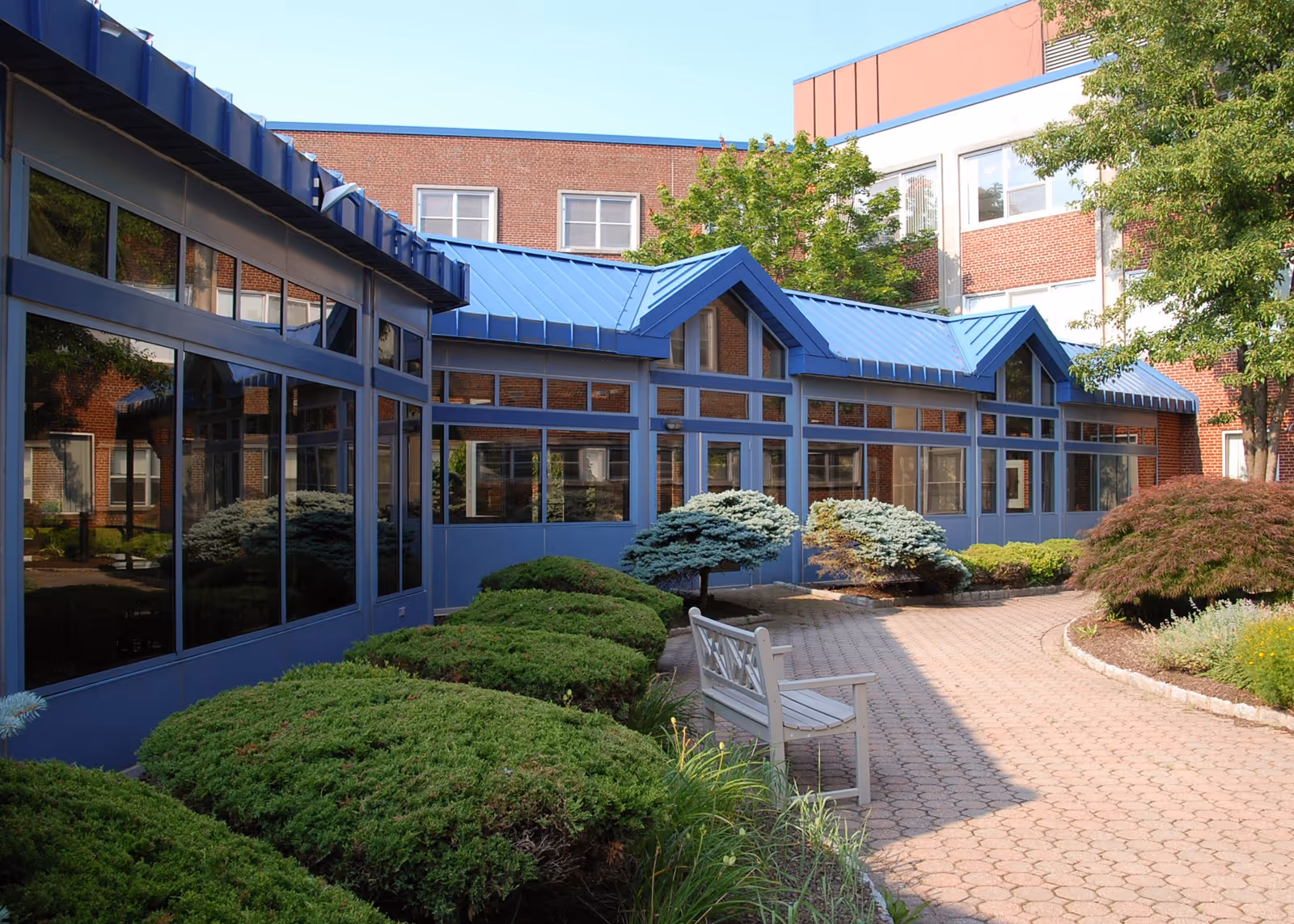 Blue-roofed glass-walled nursing home exterior with walkway and bench