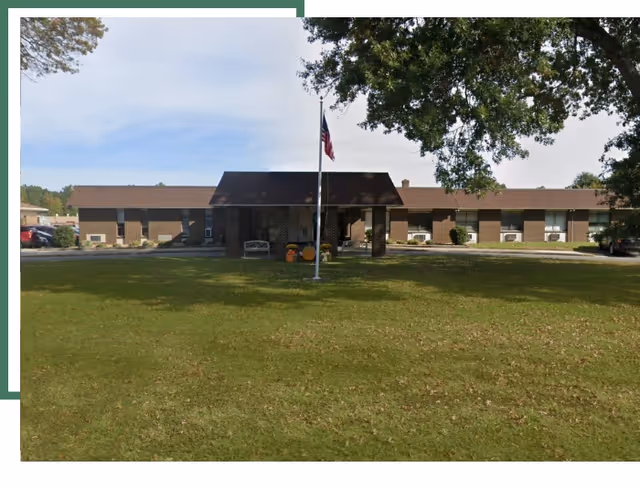 Single-story brick senior living center with flagpole, entrance canopies, and a grassy front lawn.