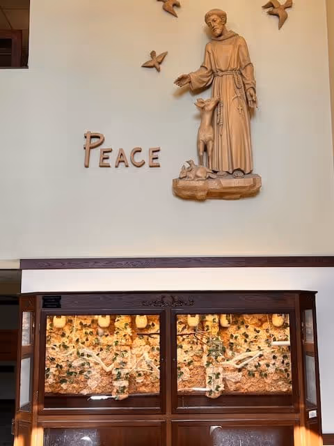 Lobby wall featuring a wooden statue of a saint above the word "PEACE" with illuminated display cabinets beneath.
