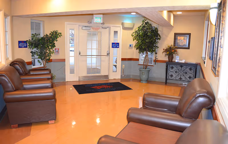 Lobby seating area with leather chairs, potted plants, and double glass entrance doors.