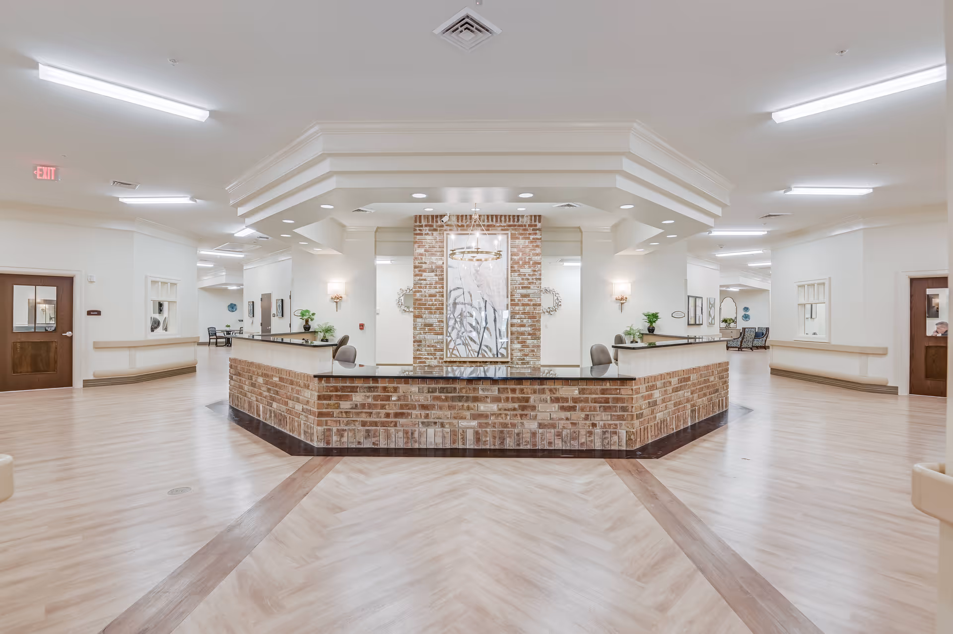 Spacious reception lobby with a central brick front desk, light wood flooring, and bright overhead lighting.