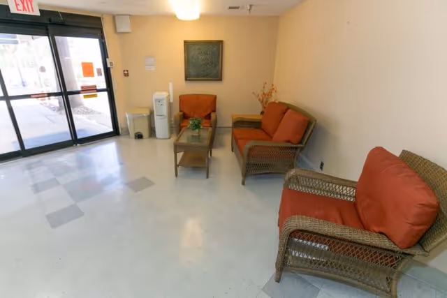 Lobby with wicker chairs and orange cushions near a glass entrance door.