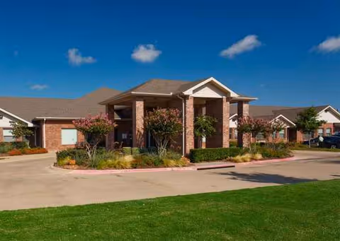 Exterior view of Town East Village front entrance with brick columns and landscaped grounds.