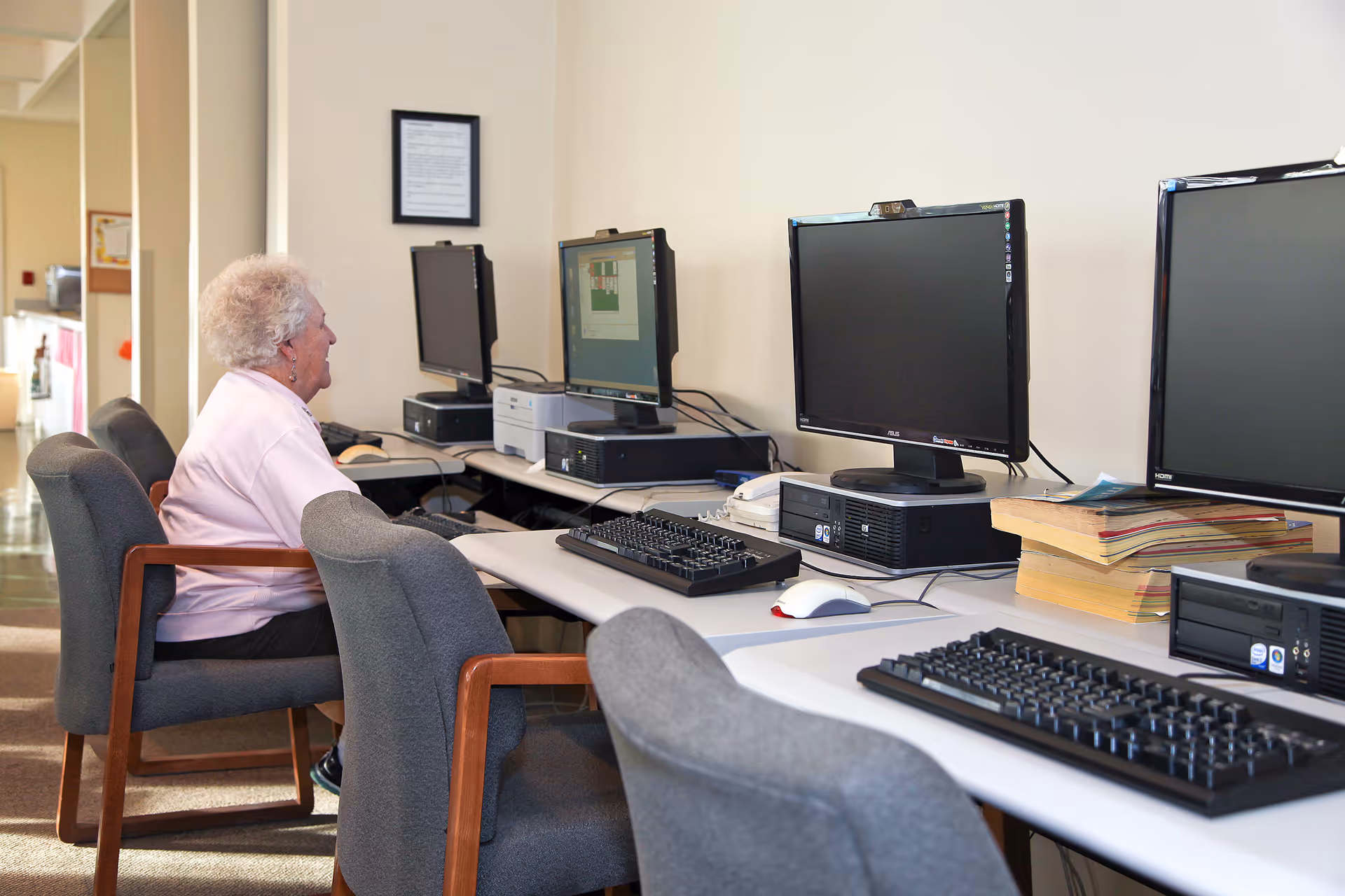 A woman sits at a row of desktop computers in a communal computer room.