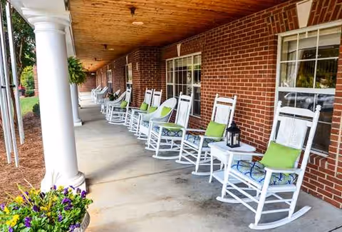 Covered brick porch with white rocking chairs, lime-green cushions, lanterns, and potted flowers.