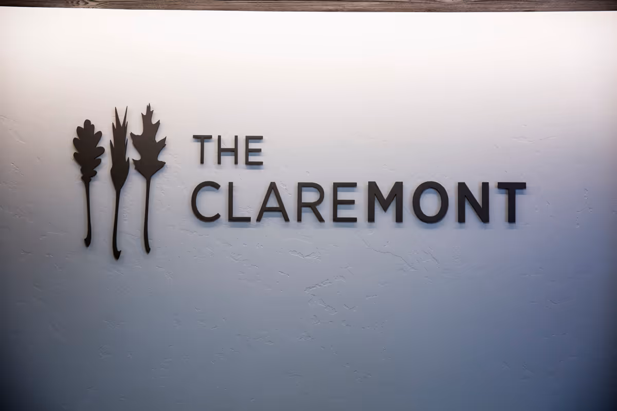 A wall with a textured white surface featuring a decorative sign that reads 'THE CLAREMONT' with three stylized leaf shapes to the left of the text.