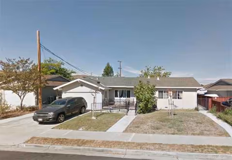 Single-story building with a driveway, parked car, and small front lawn.