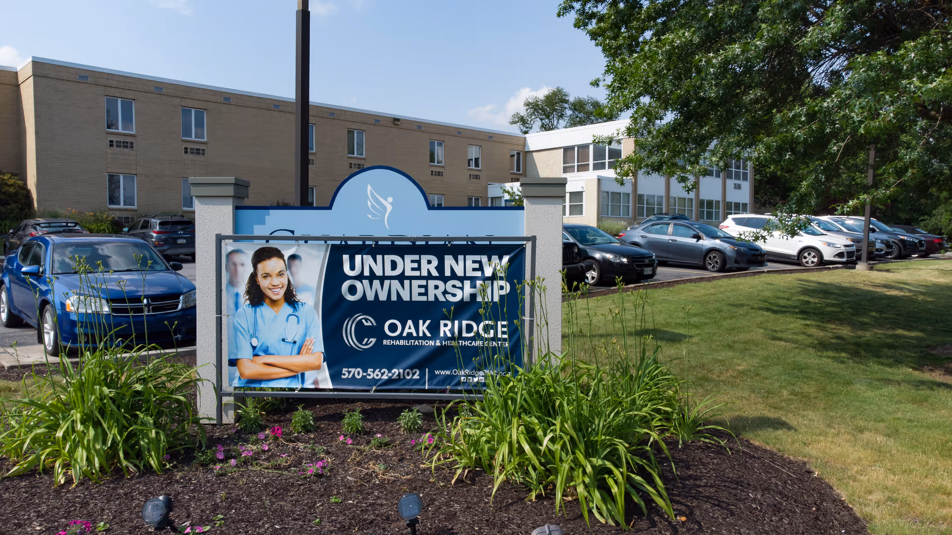 A sign reading "Under New Ownership" and "Oak Ridge Rehabilitation and Healthcare Center" with the facility building and parked cars behind it.