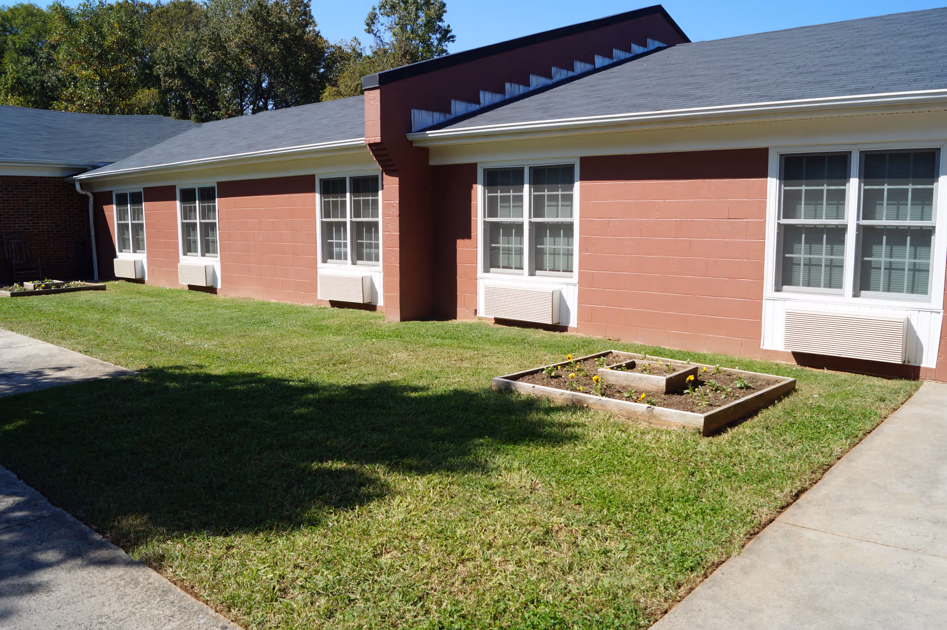 Exterior courtyard with grass, raised garden beds, and a single-story brick building with multiple windows and window air units.