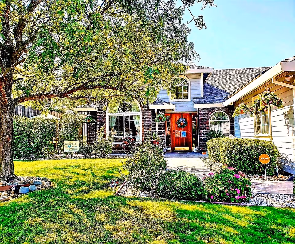 Front exterior of a single-story home with a red door, arched windows, hanging plants and a green lawn.