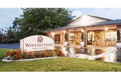 The Whitney Oaks Care Center building entrance with a lit sign and landscaping.