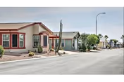 Row of single-story desert-style homes along a paved street with xeriscape landscaping and a leaning cactus.