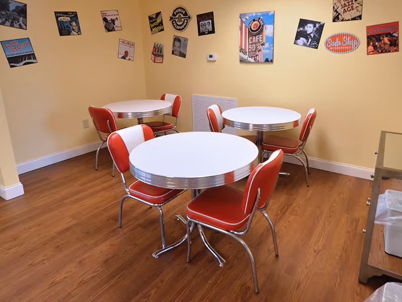 Small retro-style dining room with three round white tables and red vinyl chairs and vintage posters on yellow walls.