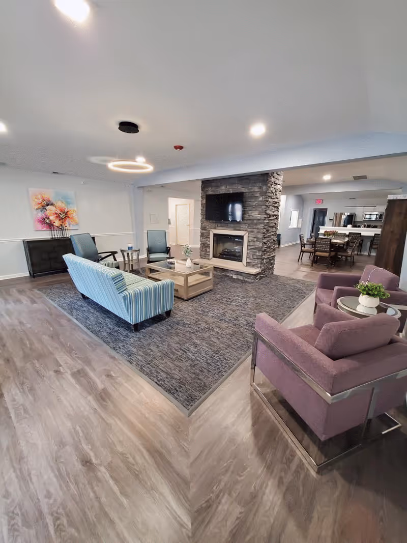 Spacious common living area with seating, a stone fireplace and wall-mounted TV, and a dining area visible in the background.