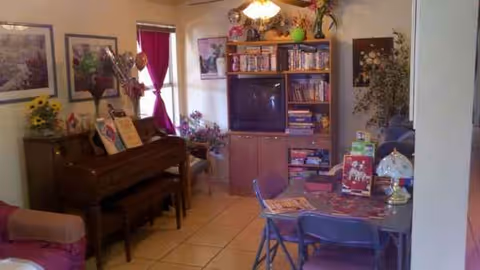 Cozy indoor living room at Westfield Assisted Living with piano, TV, bookshelf, and dining table.