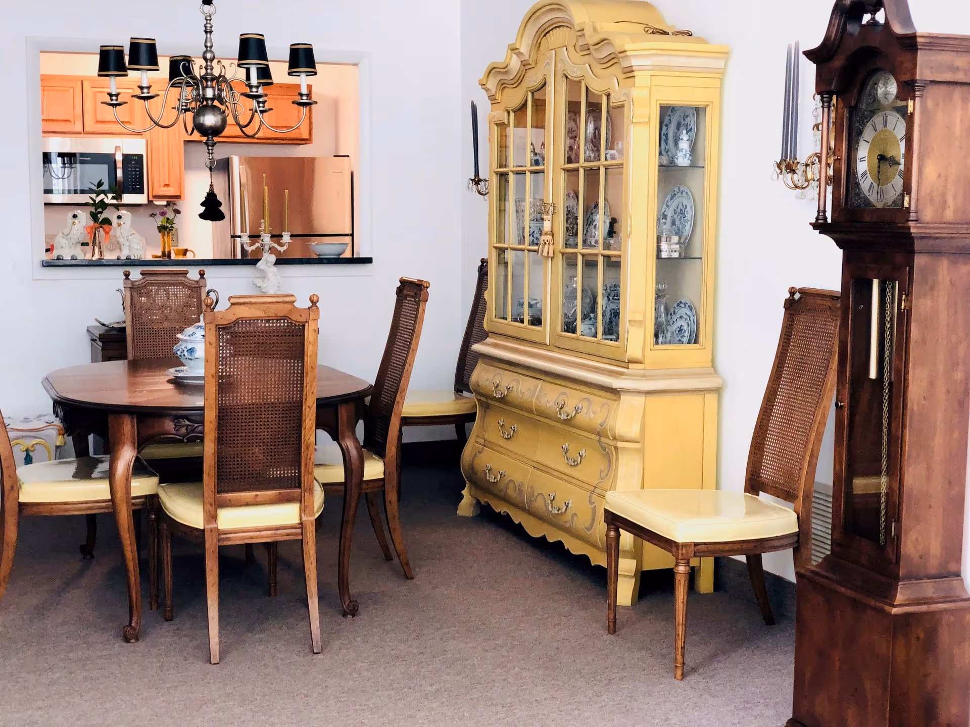 Dining room with a wooden table and cane-back chairs, a yellow china cabinet displaying dishes, and a grandfather clock.